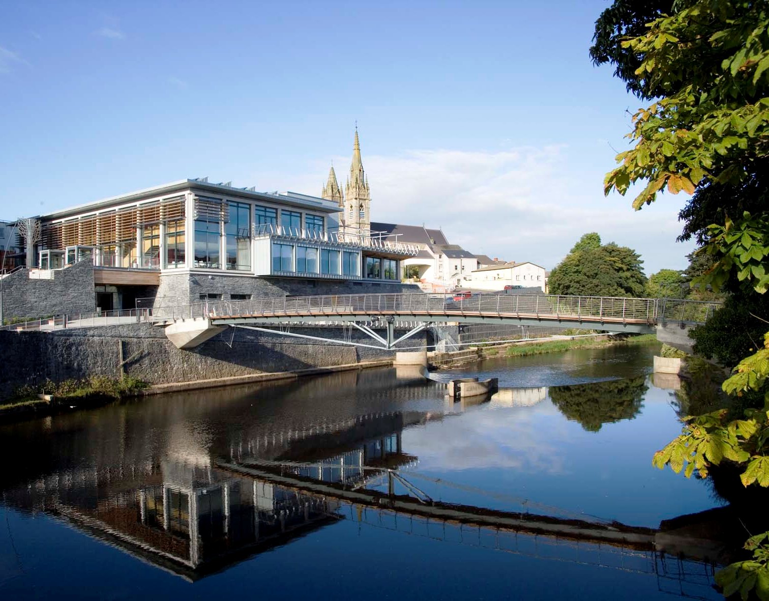 Modern architecture of the Strule Arts Centre in Omagh, Northern Ireland, with large glass windows reflecting the sky, by a river.